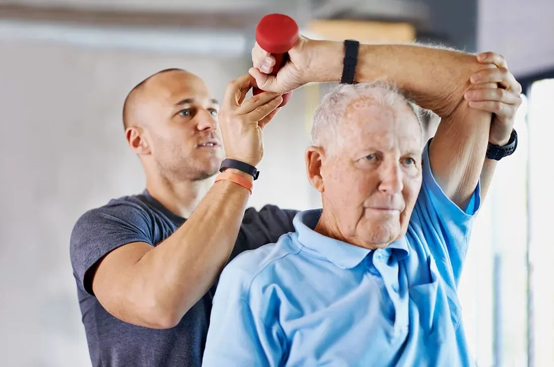 Therapist helping elderly man lift a dumbell behind his head