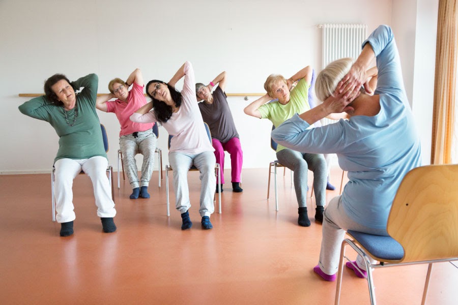 wall yoga for seniors - seniors sitting in chairs doing simple yoga pose