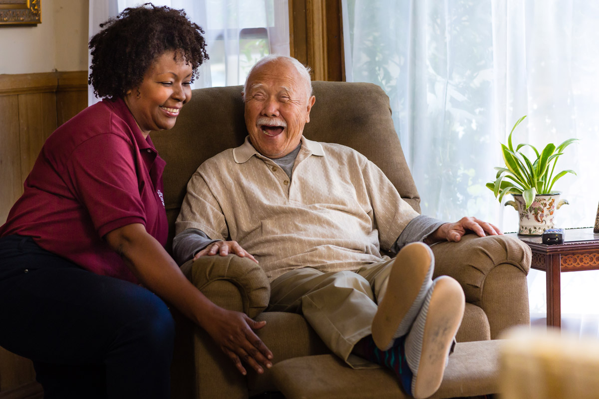 find a good caregiver - smiling woman sitting with elderly man reclined in chair