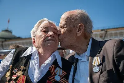 Elderly veteran man kissing elderly veteran woman on cheek