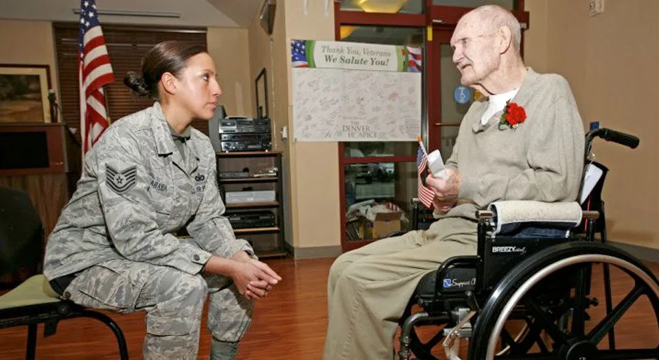 Elderly man in wheelchair talking to a female soldier 