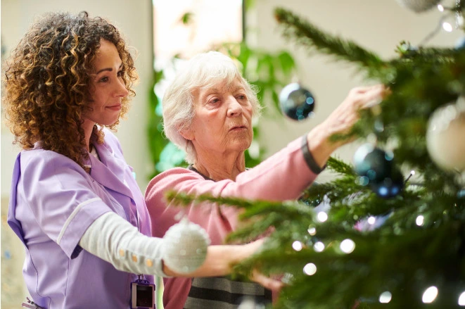 Christmas gifts for elderly - Caretaker helping elderly woman put ornaments on a christmas tree