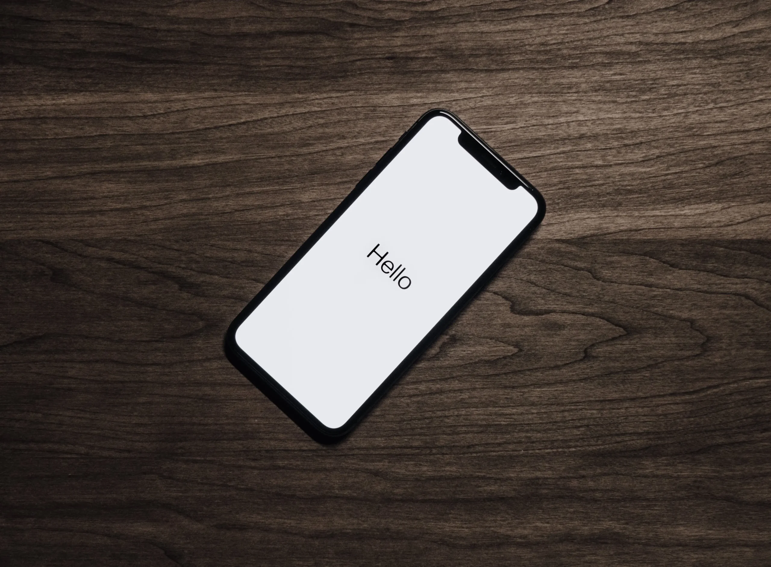 Phone sitting on table with white screen displaying the words "hello"