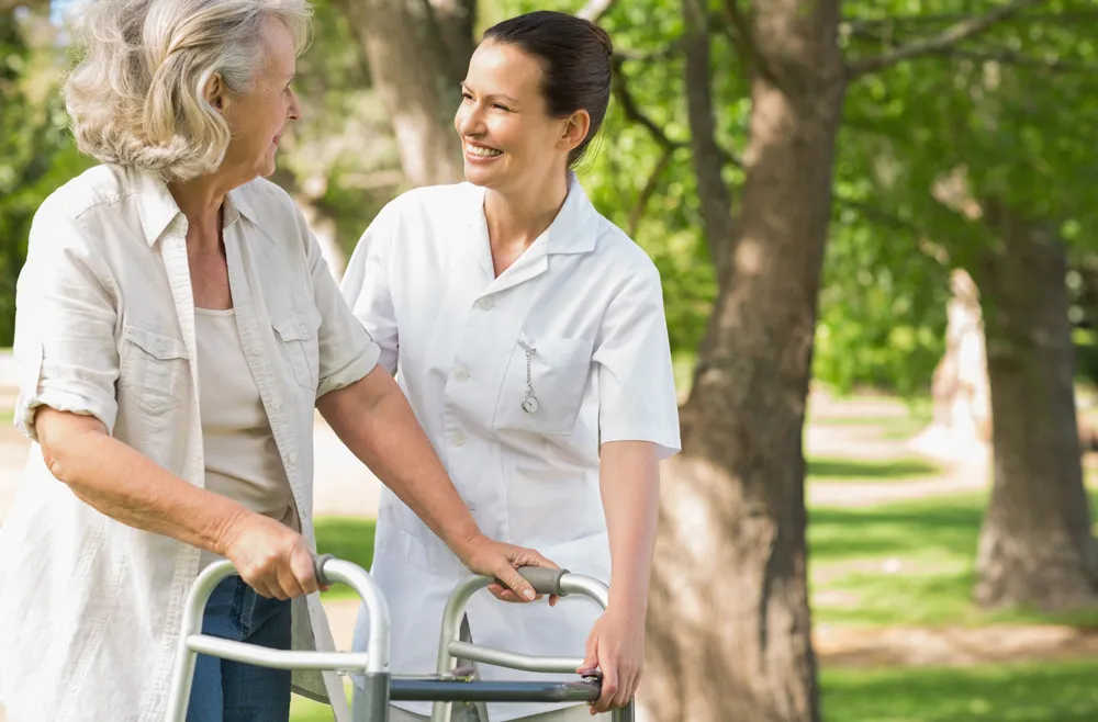 Rehabilitation Home Care Services - Elderly woman using walker after surgery with female caregiver walking alongside her in a park