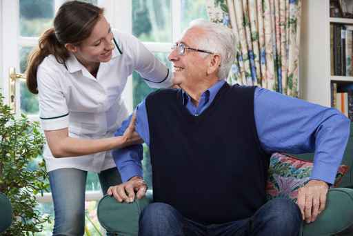 Care Worker Helping Senior Man To Get Up Out Of Chair Care Worker Helping Senior Man To Get Up Out Of Chair
